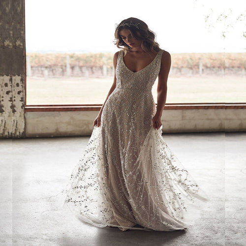 A woman wearing a bronze, V-neck, floor-length gown with beaded, sparkly leaf patterns on sheer tulle.