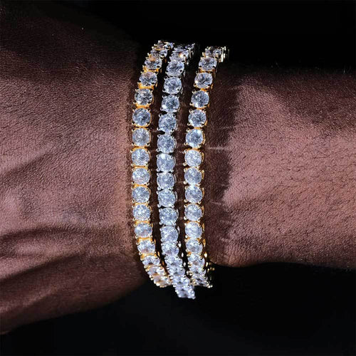 Three gold tennis bracelets with round-cut sparkling diamonds on a wrist.