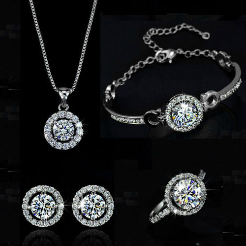Silver jewelry set with sparkling round gemstones, including a necklace, bracelet, earrings, and ring.