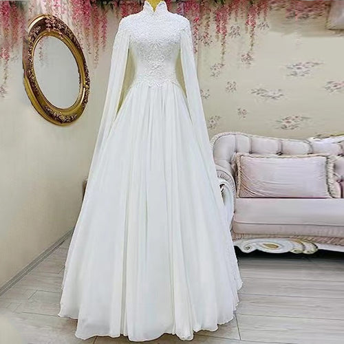 White lace high-neck wedding dress on a mannequin, featuring flowing cape sleeves and a full skirt.