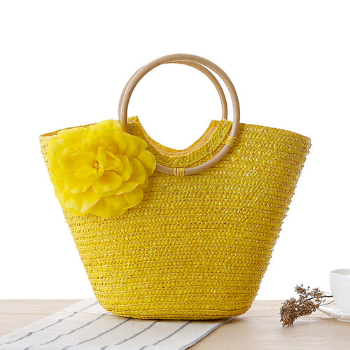 Yellow woven straw beach bag with round wooden handles and a large yellow fabric flower on the front.