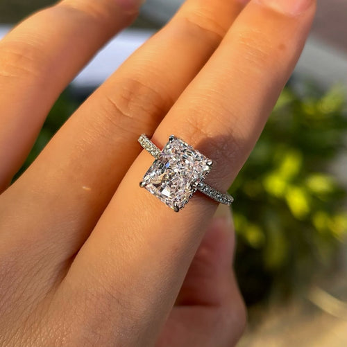 A silver ring with a large rectangular cut diamond and smaller stones on the band, worn on a finger.
