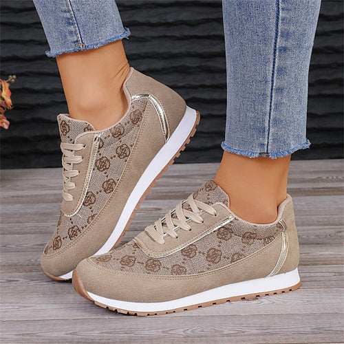 Beige lace-up sneakers with brown floral pattern, white midsoles, and silver metallic trim worn with jeans.