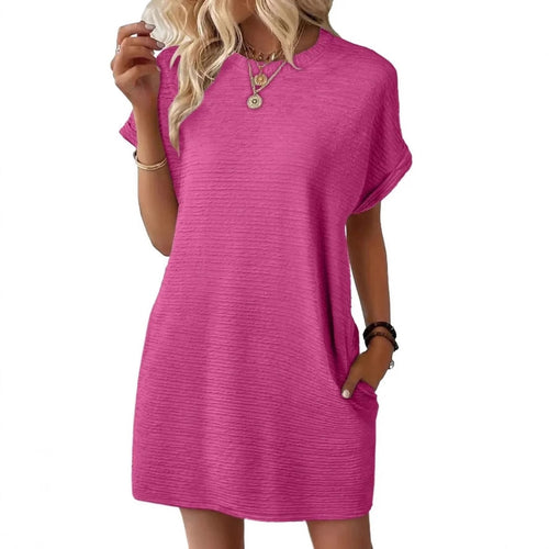 A woman wearing a textured, fuchsia pink shift dress with short sleeves and pockets.