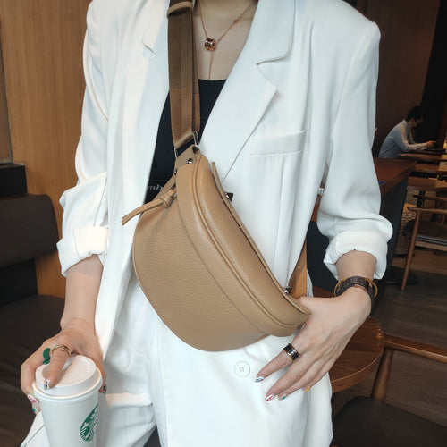 A person wearing a curved brown leather shoulder bag with a wide fabric strap.