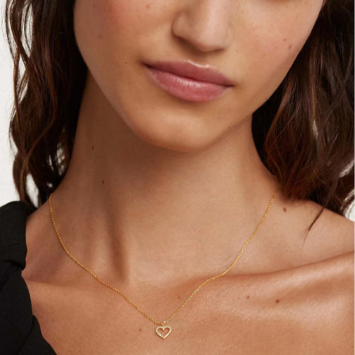 A delicate gold chain necklace with a small, pavé-set diamond heart pendant worn on a woman.