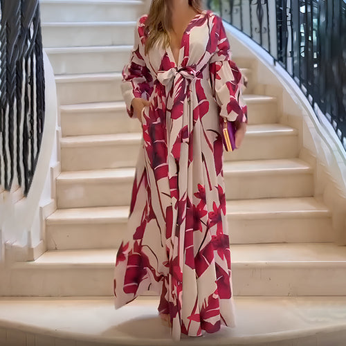 A woman wearing a long, white and pink floral dress with a bow on a white staircase.