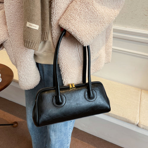 Black leather rectangular shoulder bag with dual top handles held by a person.