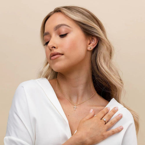 A blonde woman wearing a gold chain necklace with a small diamond-studded cross pendant.