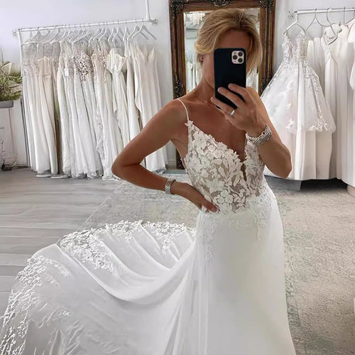A blonde woman takes a mirror selfie wearing a white satin wedding dress with lace bodice, spaghetti straps, and a long train.