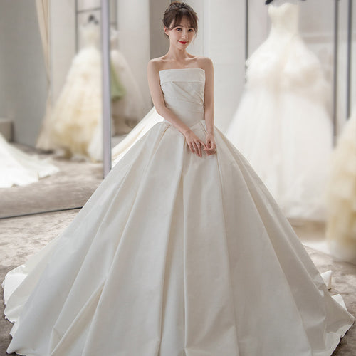A woman in a white satin strapless ball gown with a voluminous pleated skirt.