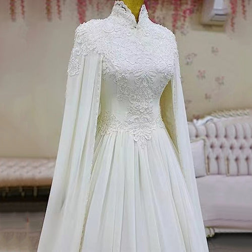 White lace wedding dress with high collar, beaded bodice, and attached cape on a mannequin.