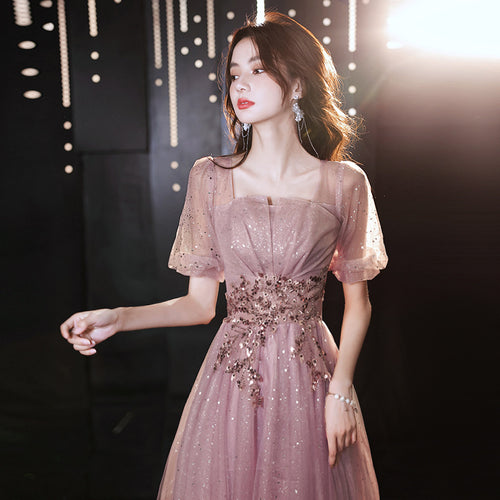 A woman wearing an elegant, sparkling pink evening gown with sheer puff sleeves and floral sequin embellishments on the waist.