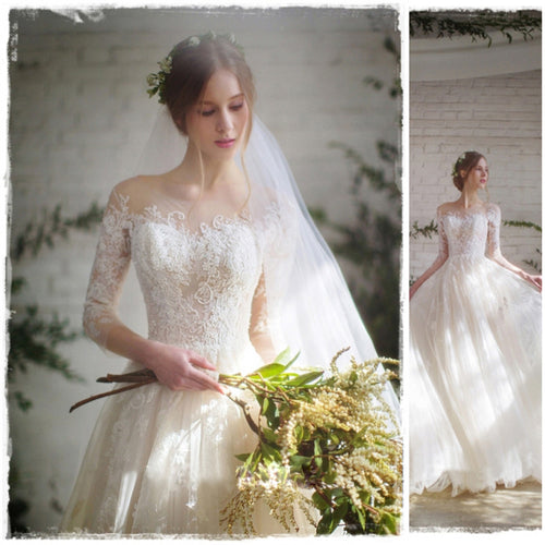 White wedding dress with lace sleeves, sweetheart neckline, full tulle skirt, veil, and flower crown, holding bouquet.