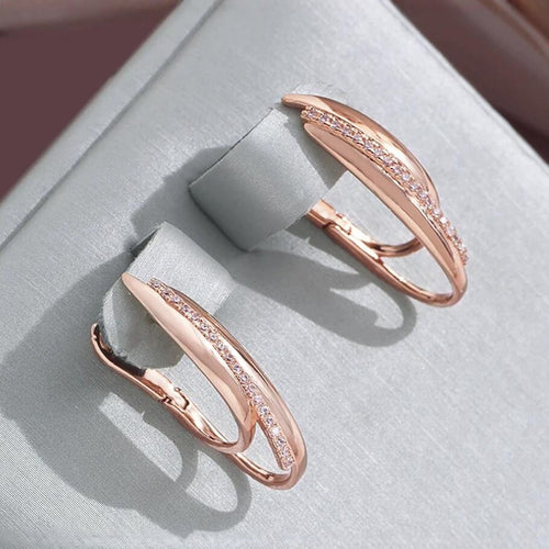 Two rose gold hoop earrings with small embedded cubic zirconia stones on a grey display.