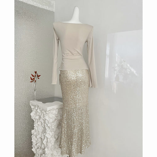 A champagne gold dress with a smooth long-sleeve top and a sequined maxi skirt on a mannequin.