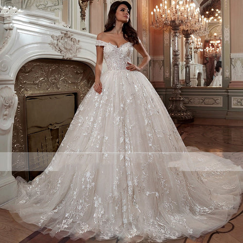 Woman wearing an off-shoulder white lace and tulle ballgown wedding dress with a long train.