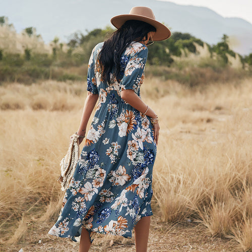 Back view of a woman wearing a blue floral V-neck dress and a wide-brimmed hat in a field.