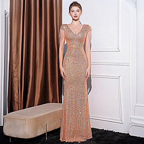 A model wearing a floor-length, fitted rose-gold sequin dress with a V-neck and beaded fringe sleeves.