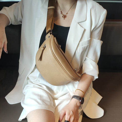 Tan leather crescent shoulder bag worn across a white blazer.