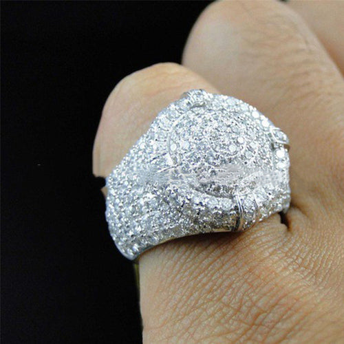 A wide silver men's ring paved with numerous small sparkling diamonds, worn on a finger.