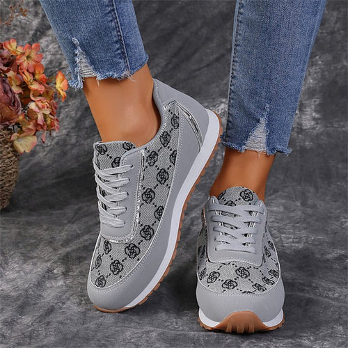 Gray lace-up sneakers with a floral pattern, white midsoles, and blue jeans on a gray backdrop.