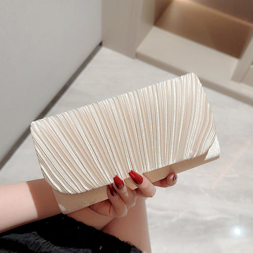 Beige pleated rectangular clutch bag held in a hand with red nails.