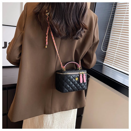 Black quilted vanity shoulder bag with pink accents and a chain strap worn by a person.